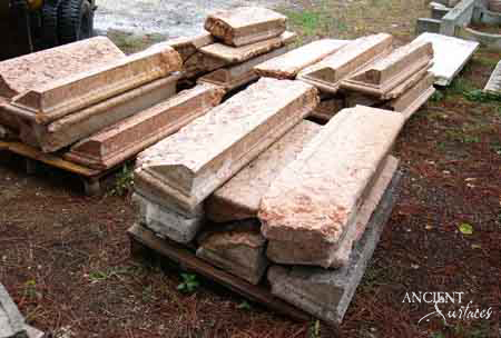 Long reclaimed antique limestone step profiles from Ancient Surfaces laid out on pallets in the yard, the stone a soft rose pink flecked with cream and fossil speckle, each length with a moulded front edge and broken ends