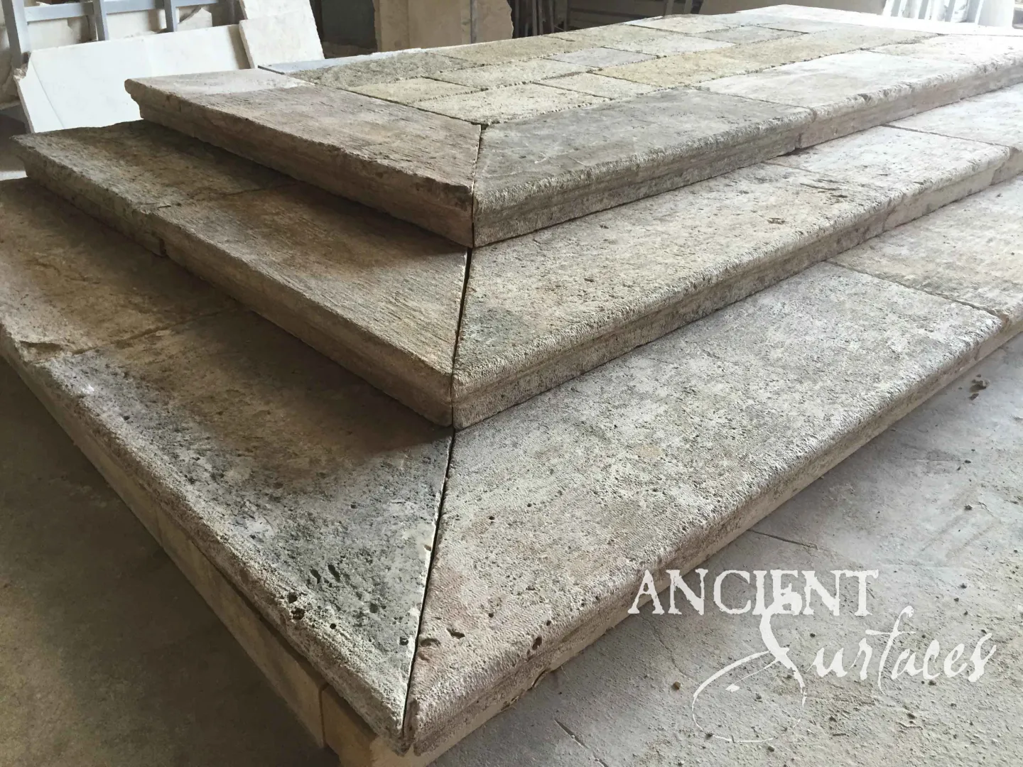 Large format reclaimed antique limestone stair treads from Ancient Surfaces stacked in the warehouse, showing their full thickness, chiselled top faces and tumbled broken edges